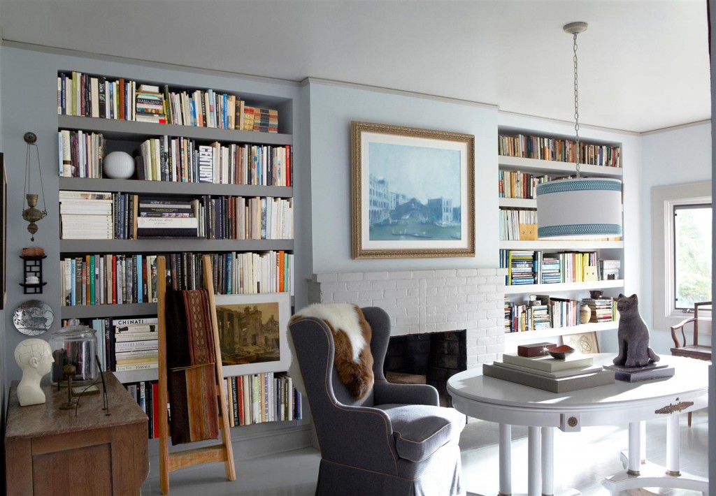 In the library, a pendant light fixture by Ro Sham Beaux hangs above a table bought at a flea market; the sheepskin throw was purchased at a charity auction, and the painting, After Tintoretto, is by Kevin Burger; the bookshelves are custom made, and the brick replace surround is painted in Benjamin Moore Aura in Lookout Point.