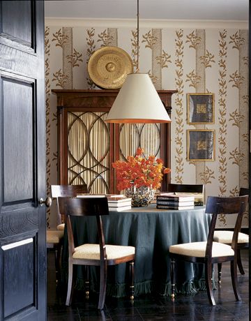 Albert Hadley: dining room has a light blue ceiling, a favorite Hadley hue for the upper plane. The American Empire mahogany armoire is topped by a Tibetan gong. Next to them are two works on paper by Connecticut artist Mark Sciarillo, also a metalworker, who made the sculpted bronze base of the living room's coffee table. The vellum lampshade, the Eyelet gold-on-ivory wallpaper, and the chairs are all Hadley's designs.