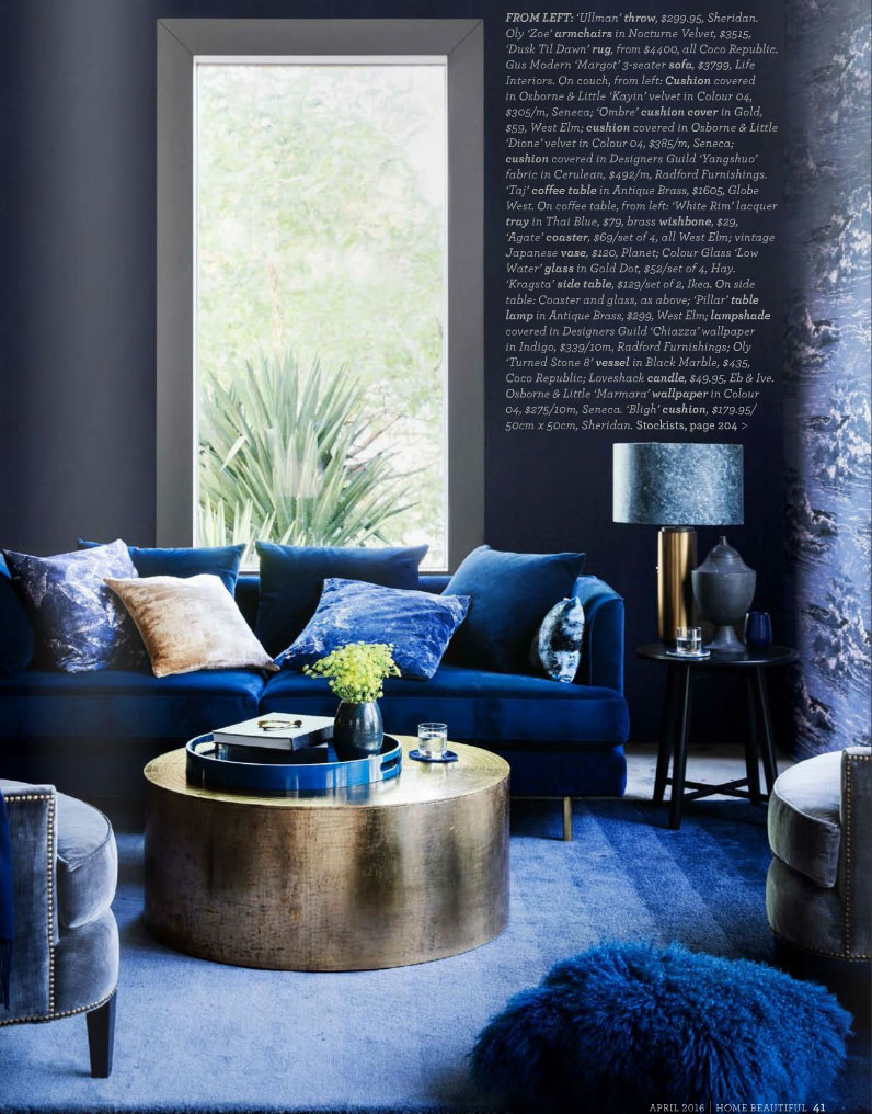 Round bronze coffee table, blue velvet sofa with an array of small square cushions, blue wallpaper from Desiigner's Guild.
