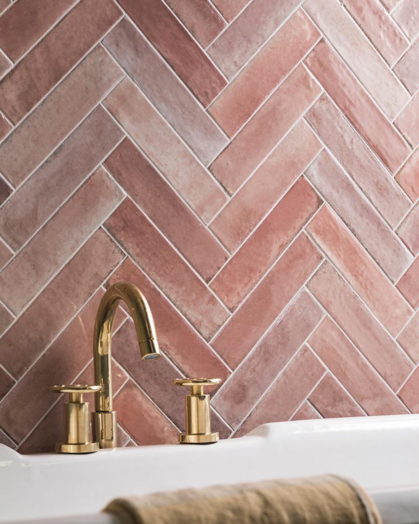 Pink porcelain tiles arranged in a herringbone pattern combined with gold hardware